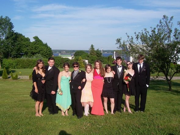 Group of teenagers in formal wear posing for a photo in a grassy field.