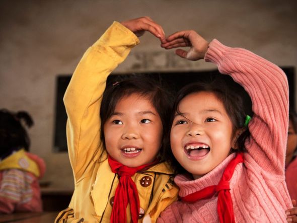 Two young girls forming a heart shape with their hands in a classroom.