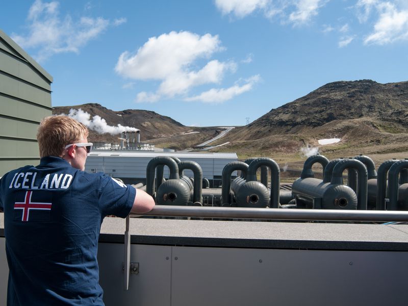 A young adult observes a geothermal power plant in Iceland, showcasing the country's commitment to renewable energy.