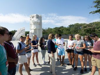 A group of teenagers visit the Martin Luther King Jr. Memorial in Washington, D.C., as their guide explains details about the memorial and its historical significance.