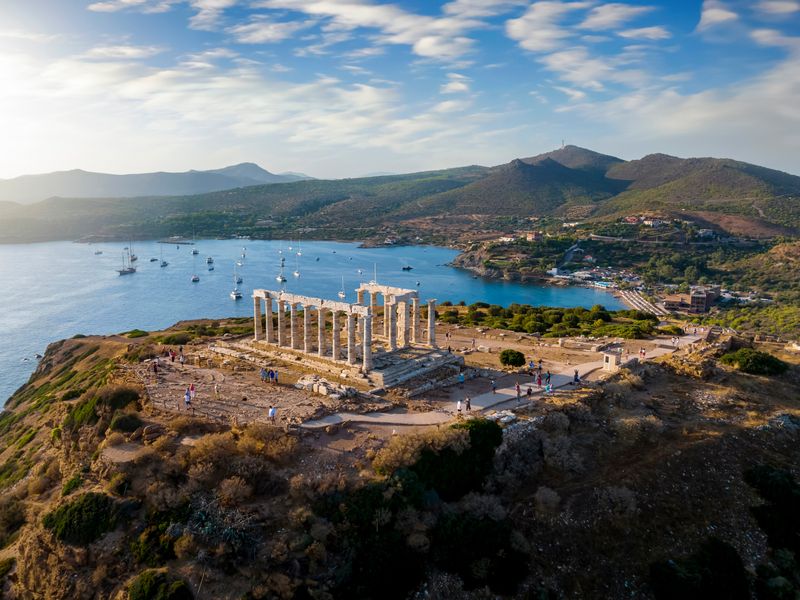 Aerial view of the Temple of Poseidon at Cape Sounion, Greece, with sailboats in the bay and the Mediterranean Sea in the background.