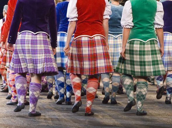 A group of Irish dancers in a line, wearing traditional kilts, performing on stage.