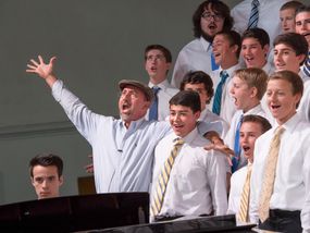 Choir director leading a group of teenage boys in song.