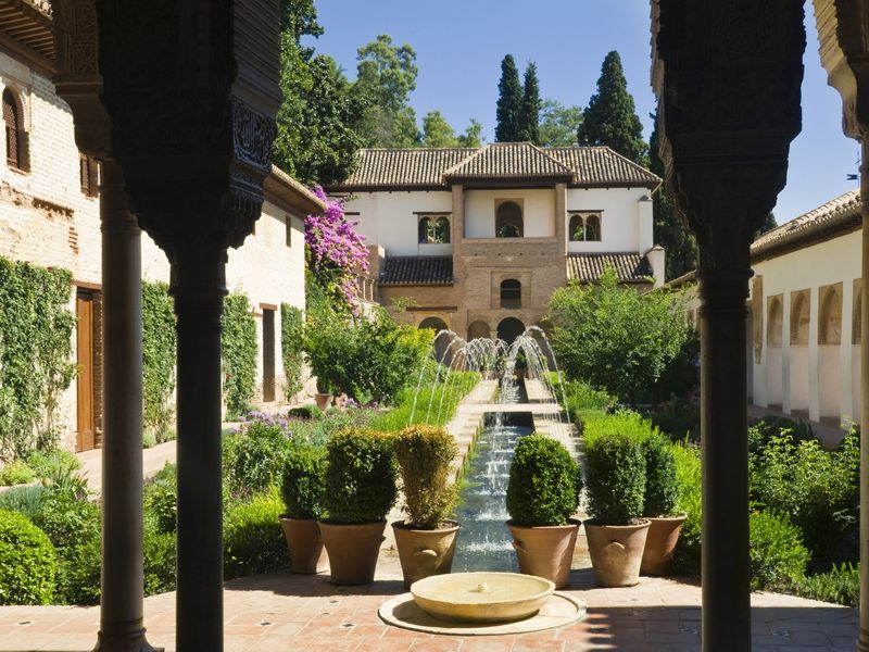 A serene courtyard garden in Granada, Spain, featuring a central fountain, manicured hedges, and vibrant bougainvillea against the backdrop of traditional Spanish architecture.