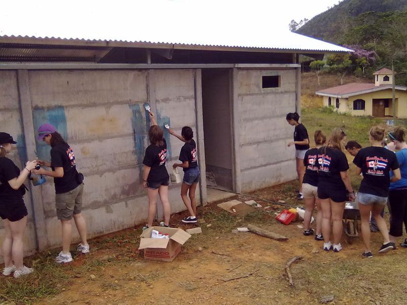 Group of young adults volunteering to paint a building in a rural community, demonstrating teamwork and community service.