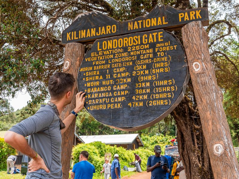 A hiker checks the sign at Londorosi Gate, the entrance to Kilimanjaro National Park.