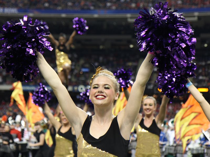 Cheerleader with purple pom-poms smiling during a performance.