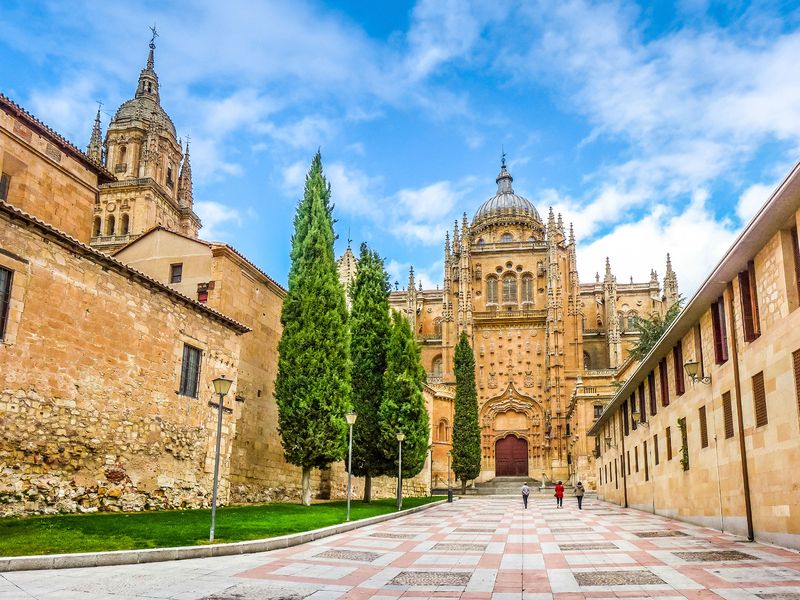 The imposing facade of the New Cathedral of Salamanca in Spain, with its intricate stonework and towering presence, stands majestically under a vibrant blue sky.