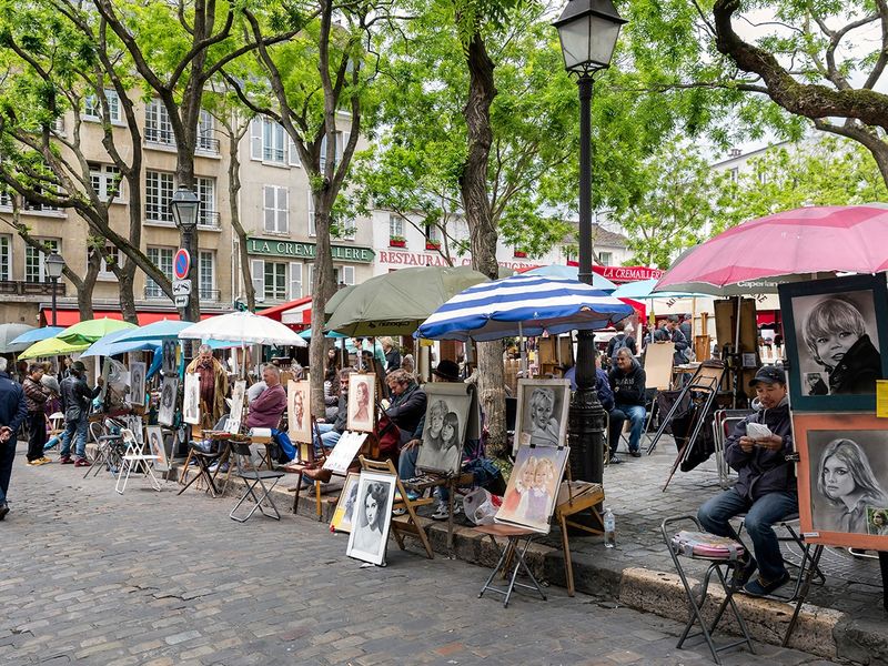 A vibrant outdoor art market in Paris, with artists displaying their work along a cobblestone street.