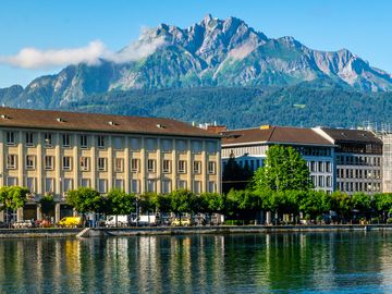 A panoramic view of the historic Chapel Bridge and Water Tower in Lucerne, Switzerland, with mountains and buildings in the background.