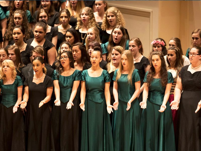 A choir of young women singing in a concert hall.