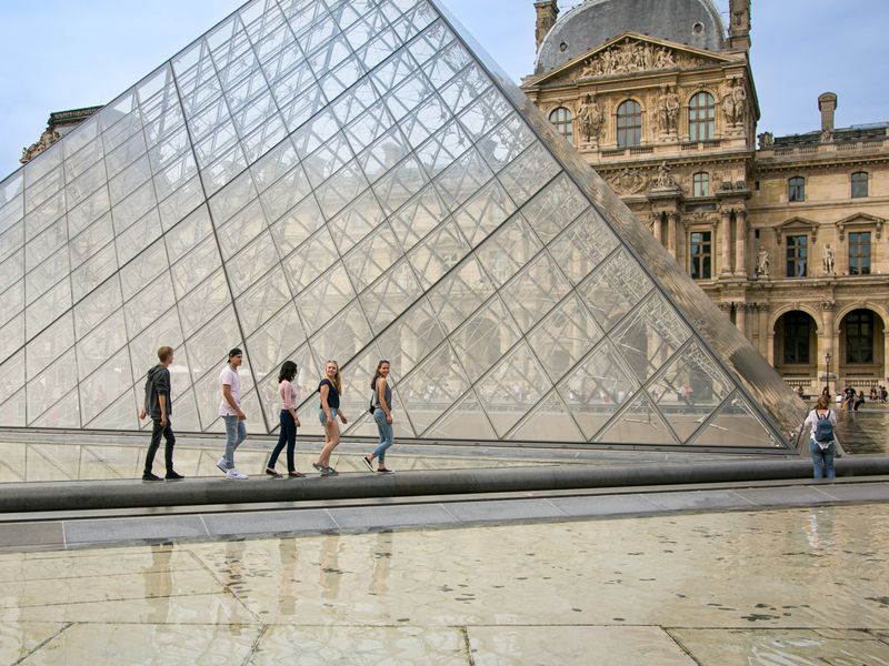 Five young adults walking in front of the Louvre Pyramid in Paris.