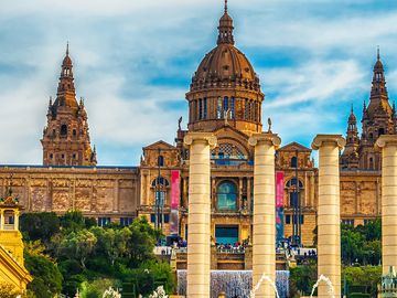 The National Art Museum of Catalonia in Barcelona, with its ornate facade and cascading fountains, set against a blue sky.