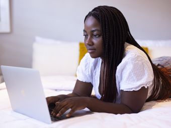 Young woman working from home on her laptop in bed