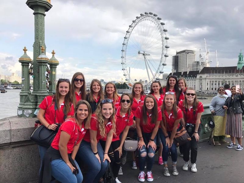 Group of young adults posing for a photo with the London Eye in the background.