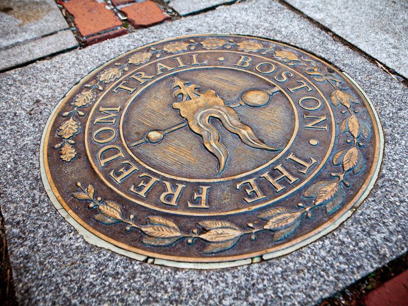 Close-up of a bronze Freedom Trail marker on a cobblestone street in Boston.