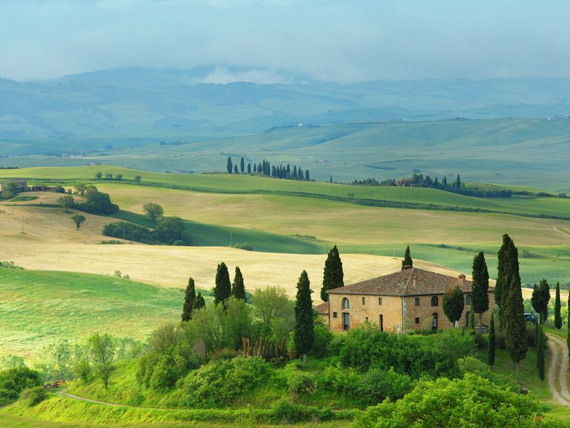 Scenic view of the Tuscan countryside with rolling green hills, cypress trees, and a farmhouse.