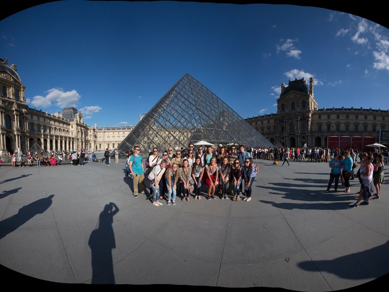 A group of young adults smiles for a photo in front of the Louvre Pyramid in Paris, France.