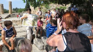 A tour guide explains the map of the Delphi ruins to a group of tourists.