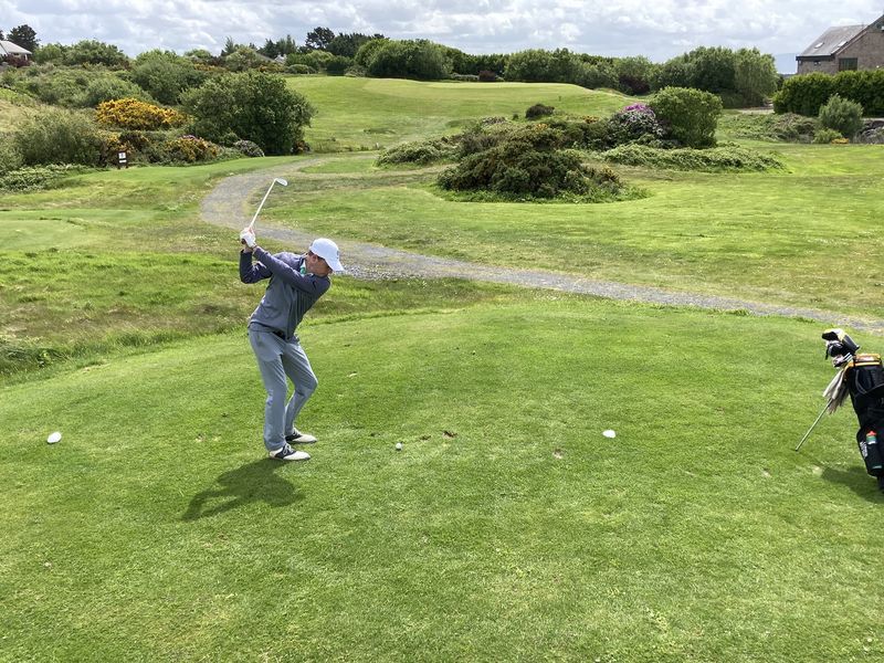 A young adult golfer takes a swing on a green golf course.