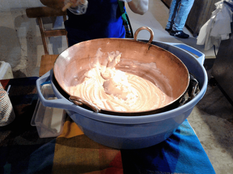 A person whisking a creamy mixture in a large copper pot.