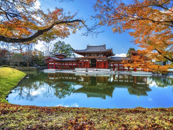 A traditional Japanese temple reflected in a pond, surrounded by colorful autumn trees.