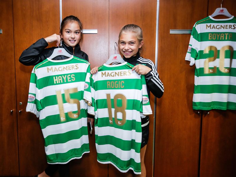 Two young girls holding Celtic FC jerseys in a locker room