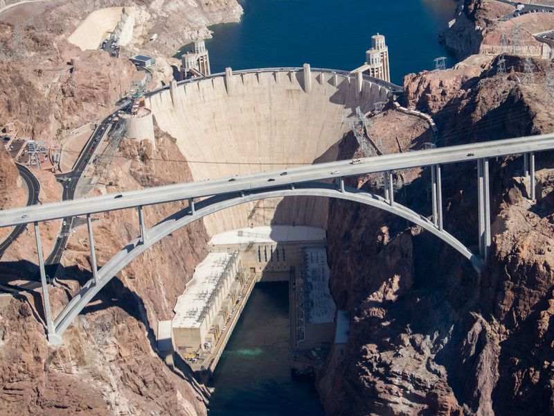 Aerial view of Hoover Dam and bridge spanning the Colorado River, showing the dam's massive concrete structure and the turquoise water of Lake Mead.