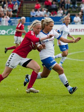 Two female soccer players competing for the ball during a game.