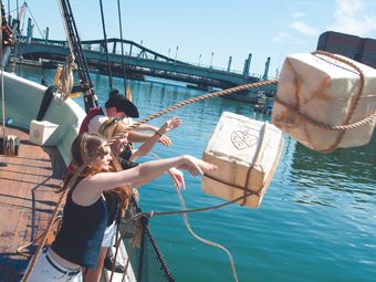 A group of people throw packages off the side of a ship into the water.