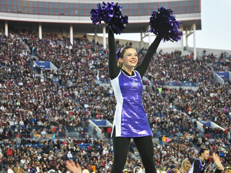 Cheerleader holding purple pom poms is performing at the Liberty Bowl