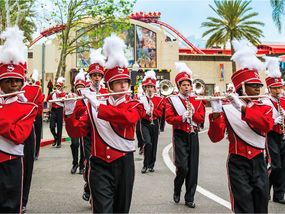 A high school marching band in red and white uniforms marches down a street at Universal Studios