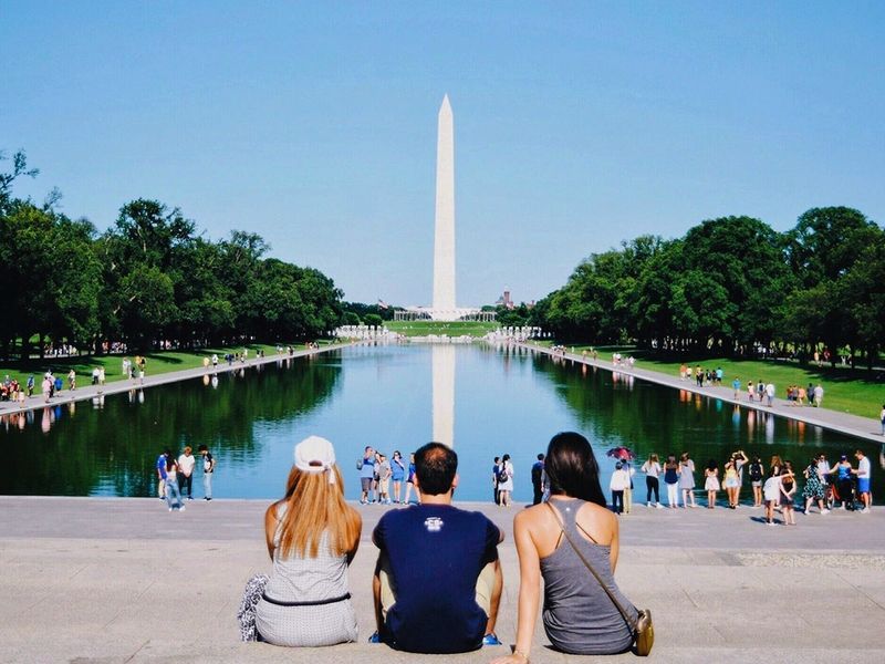 Three friends sitting on the steps of the Reflecting Pool facing the Washington Monument.