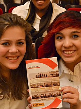 Two young women smile as they hold a Carnegie Hall playbill.