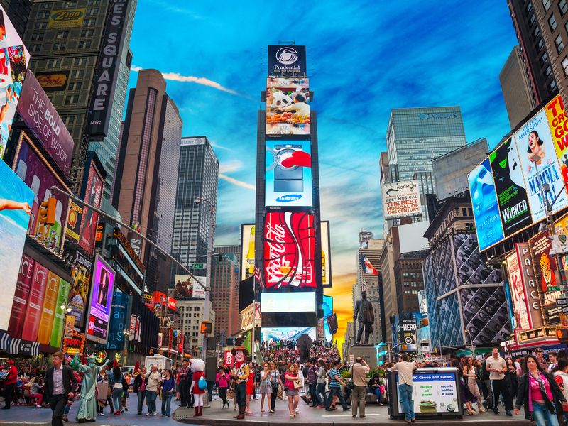 A bustling scene of Times Square in New York City at sunset, with its bright billboards illuminating the crowds and buildings.