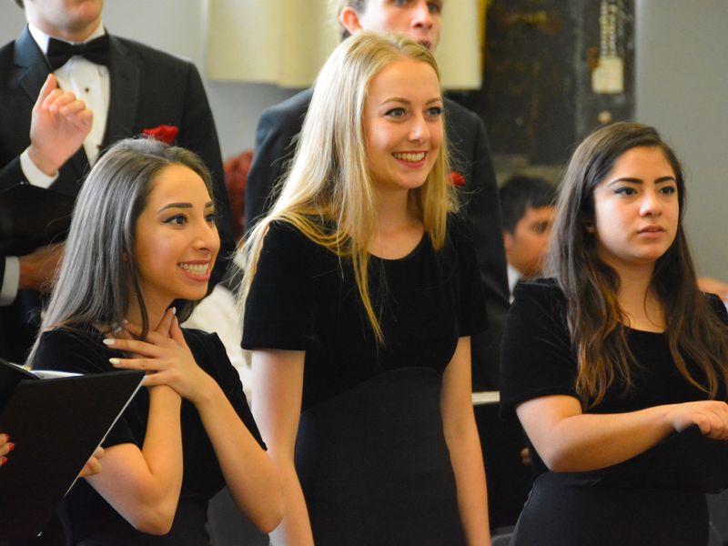 Three young female adults singing in a choir.