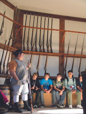 A historical reenactor describes colonial rifles to a group of teenagers at Colonial Williamsburg.