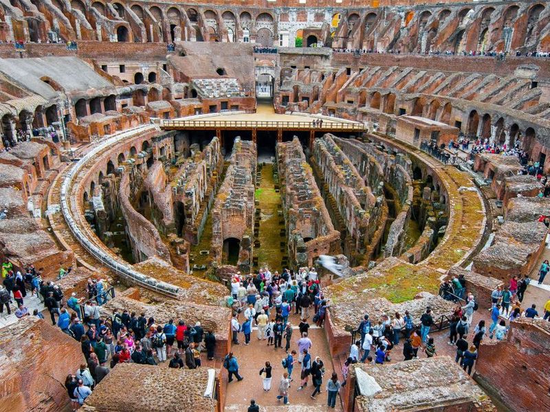 Interior view of the Colosseum in Rome, Italy, with tourists exploring the ruins beneath the arena.