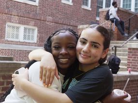 Two teenage girls hug and smile, showing their friendship.