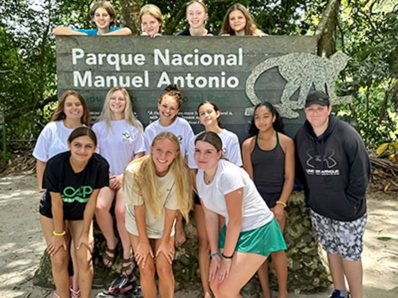 Group of teenagers at Manuel Antonio National Park entrance sign.