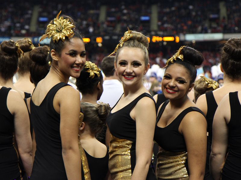 Three teenage girls on a dance team smile for the camera during a competition.