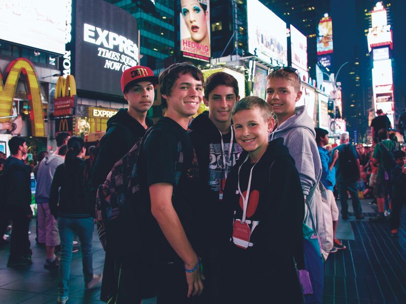 Group of teenagers and children posing for a photo in Times Square at night.