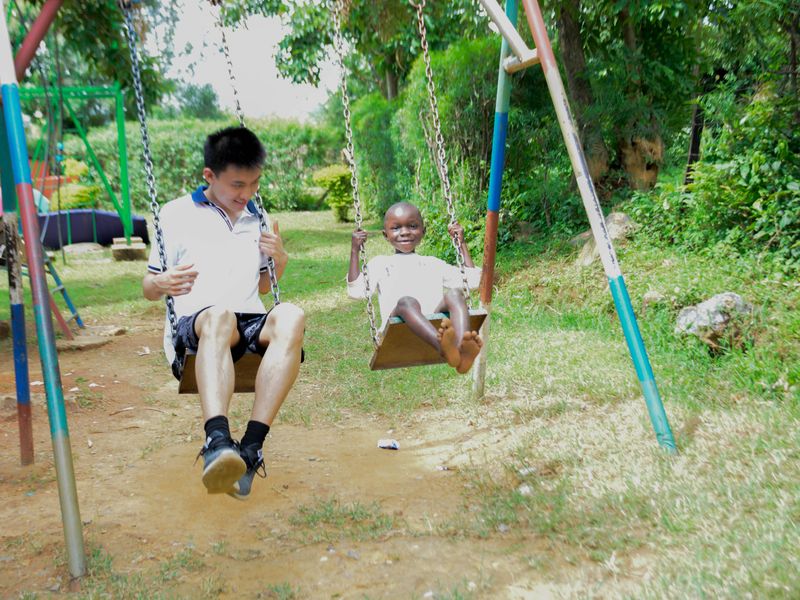 A young adult and a small child enjoy swinging together on a playground swing set.