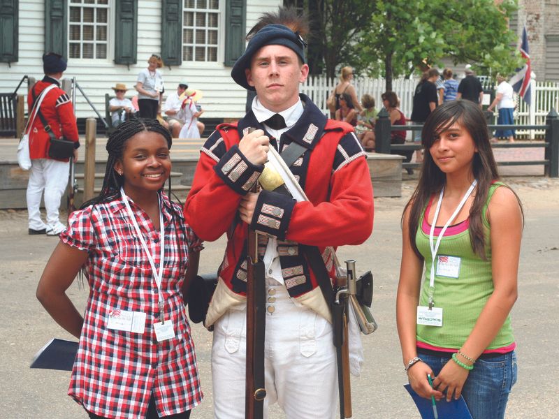 Two teenage girls flank a young man in a historical military uniform, likely at a historical reenactment or museum.