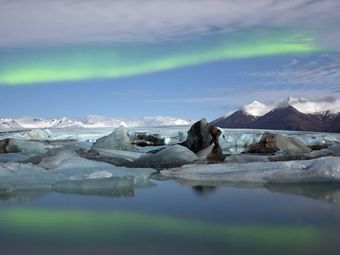 Glaciers in a lake with snow-capped mountains and the aurora borealis in the background.