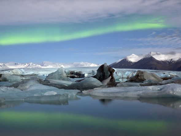 Glaciers in a lake with snow-capped mountains and the aurora borealis in the background.