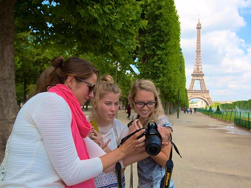 Three people viewing photos on a digital camera near the Eiffel Tower