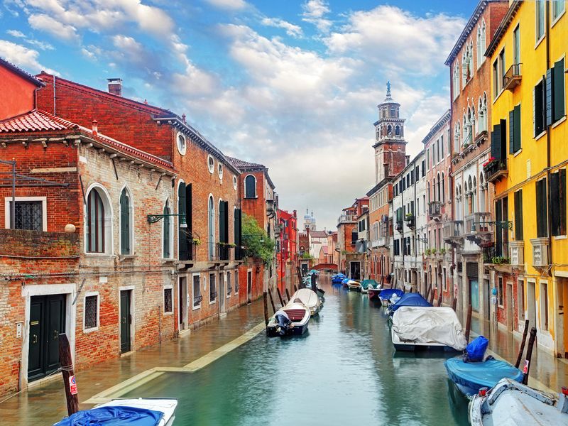 A view of a canal in Venice, Italy, with colorful buildings lining the waterway and boats moored along the sides.