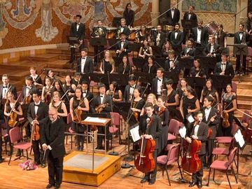 A youth orchestra performing on a stage in a grand concert hall.