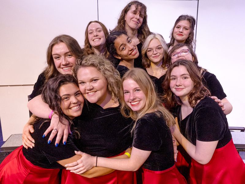 Group of young adult women smiling in matching performance outfits.